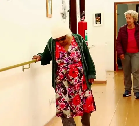 Residentes caminham pelo corredor apoiadas no corrimão