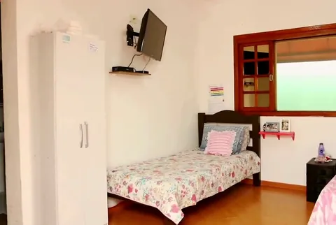 Quarto claro com duas camas arrumadas, armário, televisão e janela de madeira para o jardim