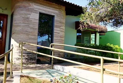 Rampa de acesso com corrimão dourado e jardim na lateral da casa
