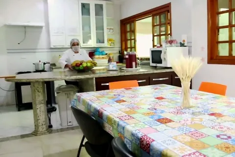 Refeitório com mesa posta, cozinha aberta e janelas de madeira