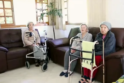 Residentes conversam nos sofás da sala de estar, com janelas amplas e luz natural